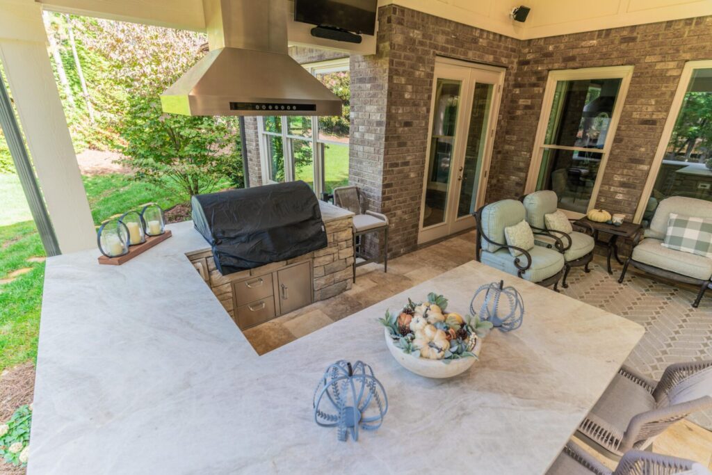 Built-in outdoor grill with stainless steel vent hood, stacked stone surround, and waterfall counter island in Mint Hill, North Carolina.