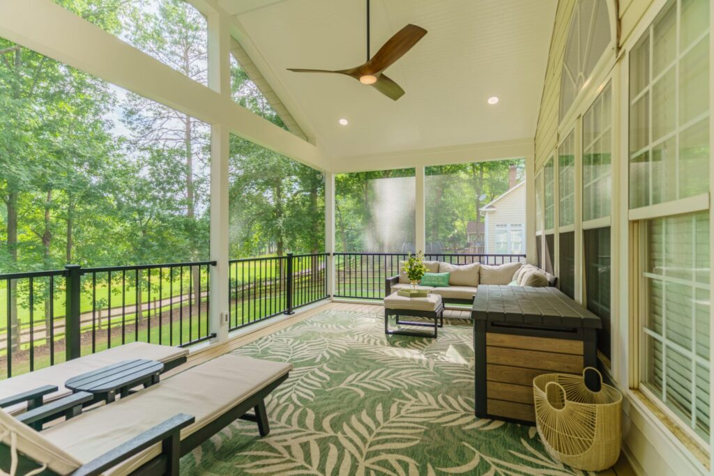 Interior view of a bright Eze-Breeze screened porch featuring TimberTech Natural White Oak flooring, black Trex aluminum railings, ceiling fan, and outdoor lounge furniture.