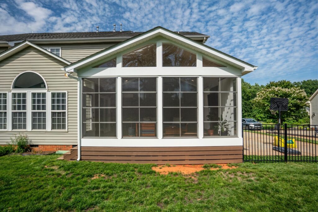 Exterior view of a white vinyl Ezebreeze screened porch addition with floor-to-ceiling multi-pane vinyl windows attached to the back of a Mint Hill house.