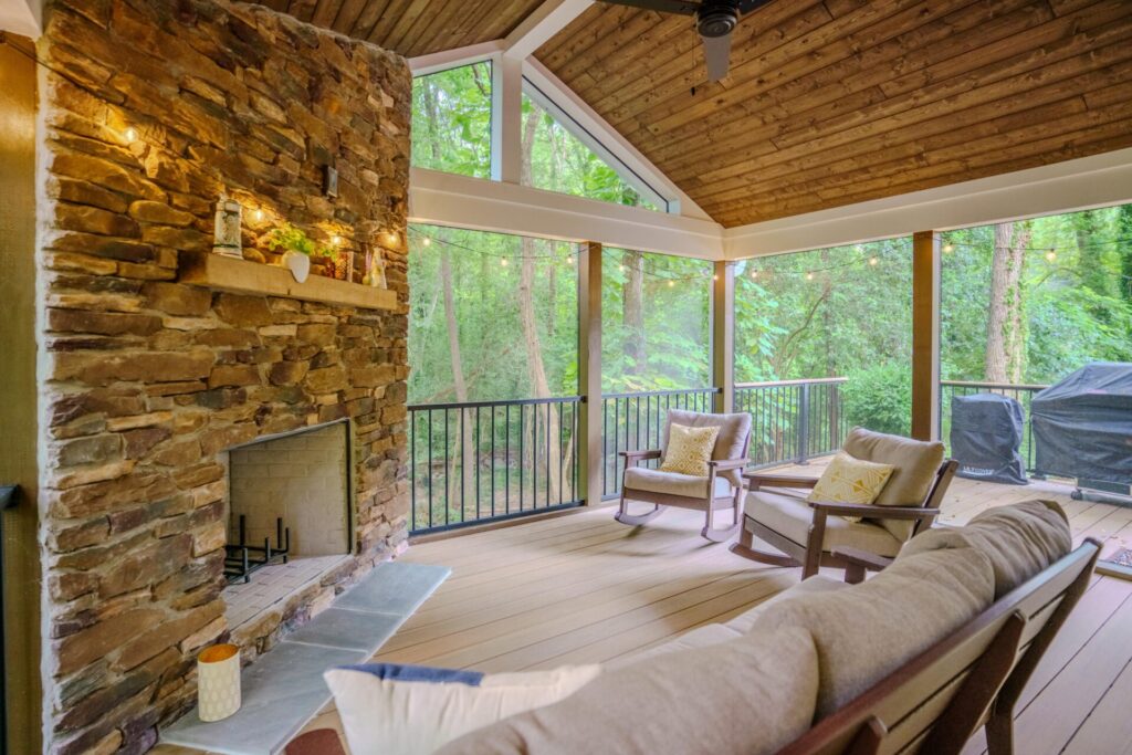 Screened-in porch in Sedgefield Myers Park with a rustic stacked stone fireplace, wood vaulted ceiling, and TimberTech Coconut Husk composite flooring.