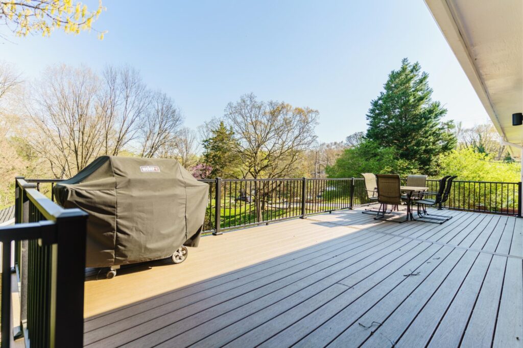 High-angle shot of a spacious composite deck using TimberTech Dark Roast boards, fitted with a black Trex aluminum railing, patio table, and covered grill.