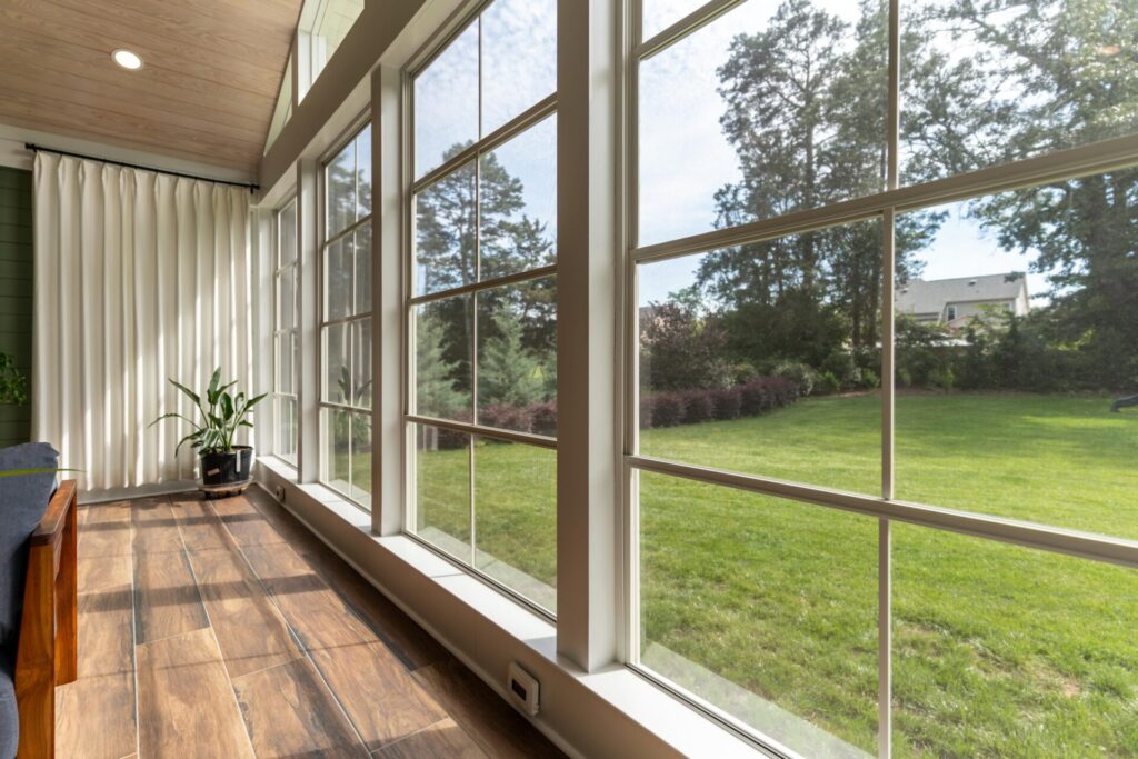 Close-up of Tobacco Cask wood-look matte porcelain tile flooring running along tall Ezebreeze porch windows overlooking a grassy backyard.