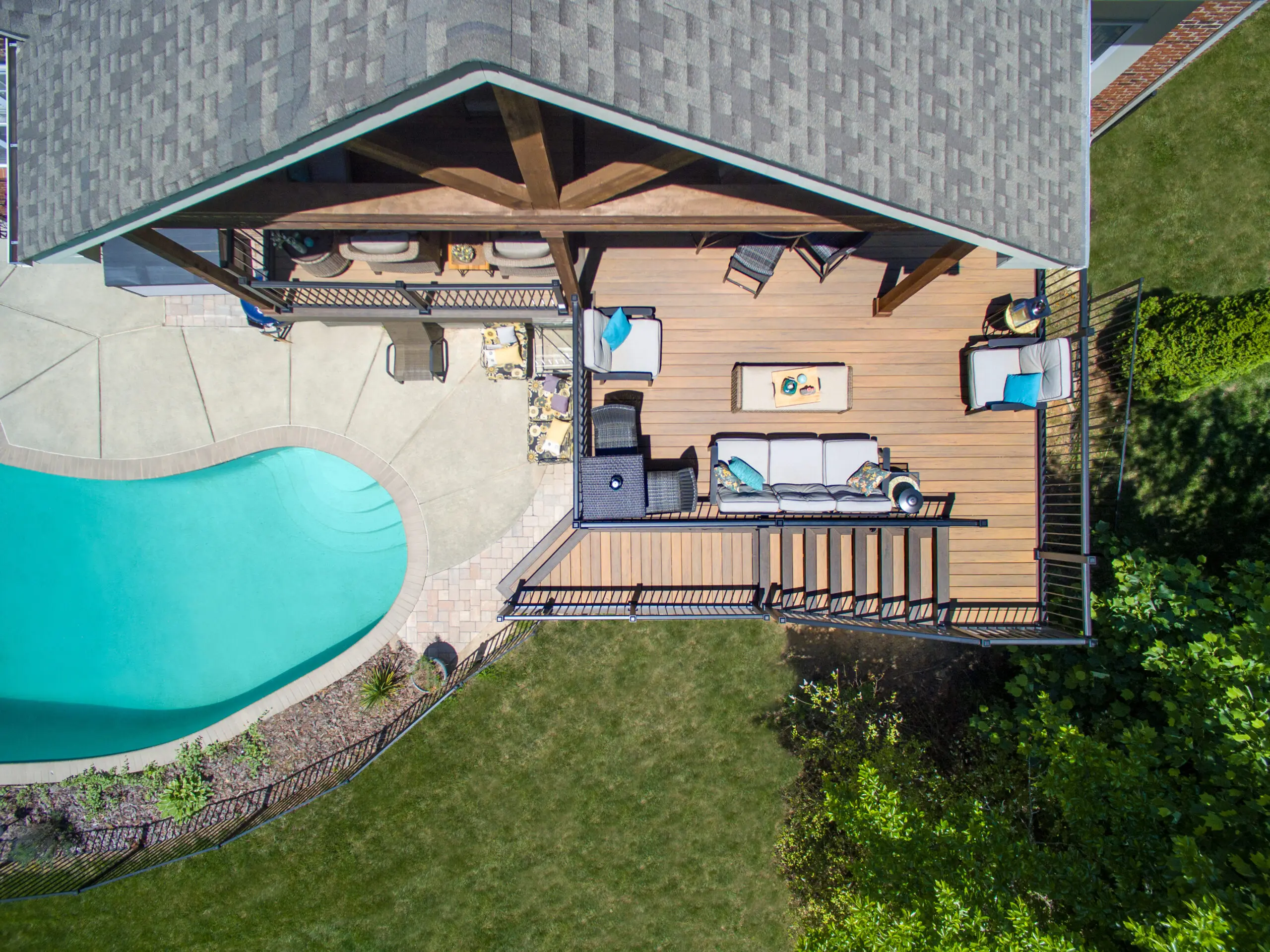 Top-down aerial view of a multi-level composite deck and timber-framed porch addition with black aluminum railings, overlooking a backyard pool and lounge area.