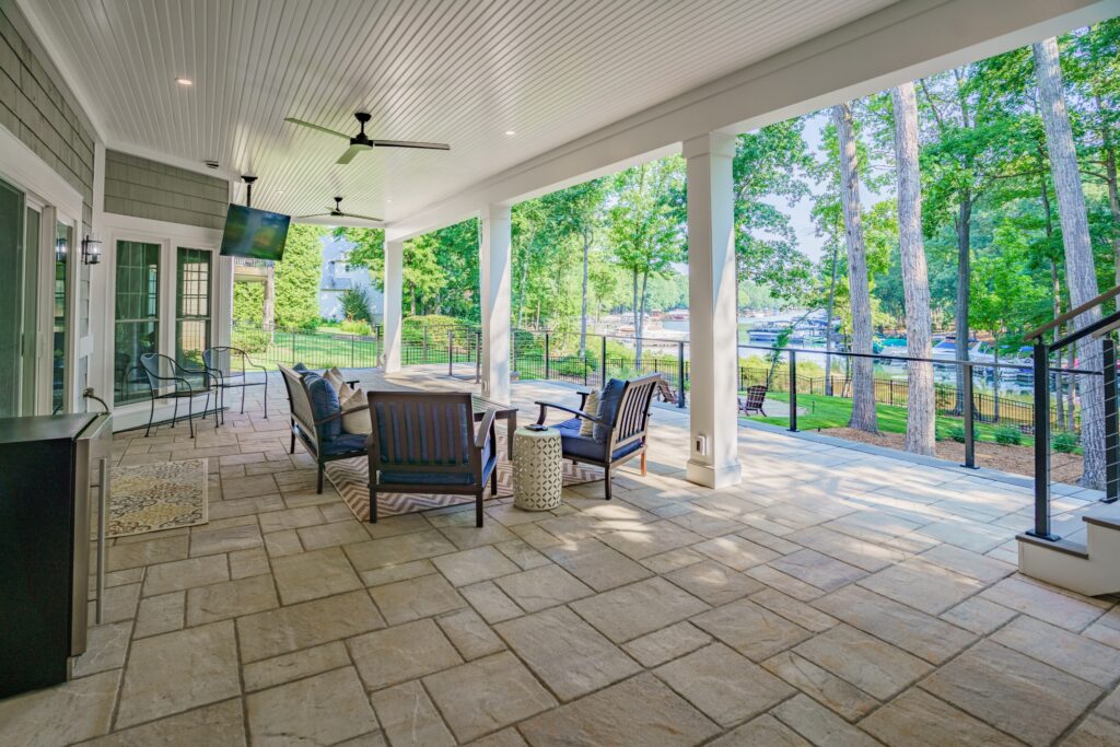 Expansive covered outdoor living space with flagstone pavers and white columns overlooking a lakeside dock.