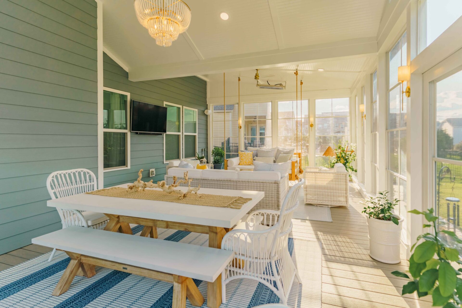 Looking across a white farmhouse-style outdoor dining table on a custom screened porch toward a cozy lounge setup, featuring open skylights and integrated ceiling heaters.