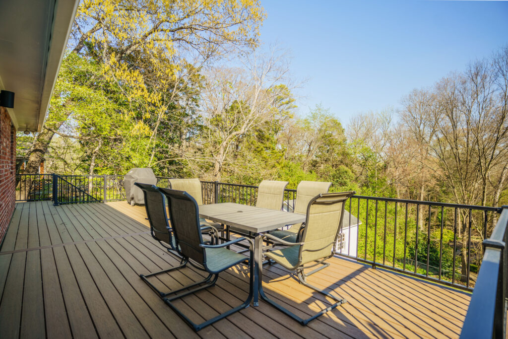 An outdoor dining table and chairs set on a new elevated composite deck built with TimberTech Dark Roast decking and black Trex aluminum railings in Charlotte's Stonehaven neighborhood.