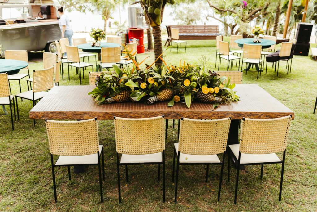 An outdoor party layout with a large wooden table, guest seating zones, and a food service area on a lawn.